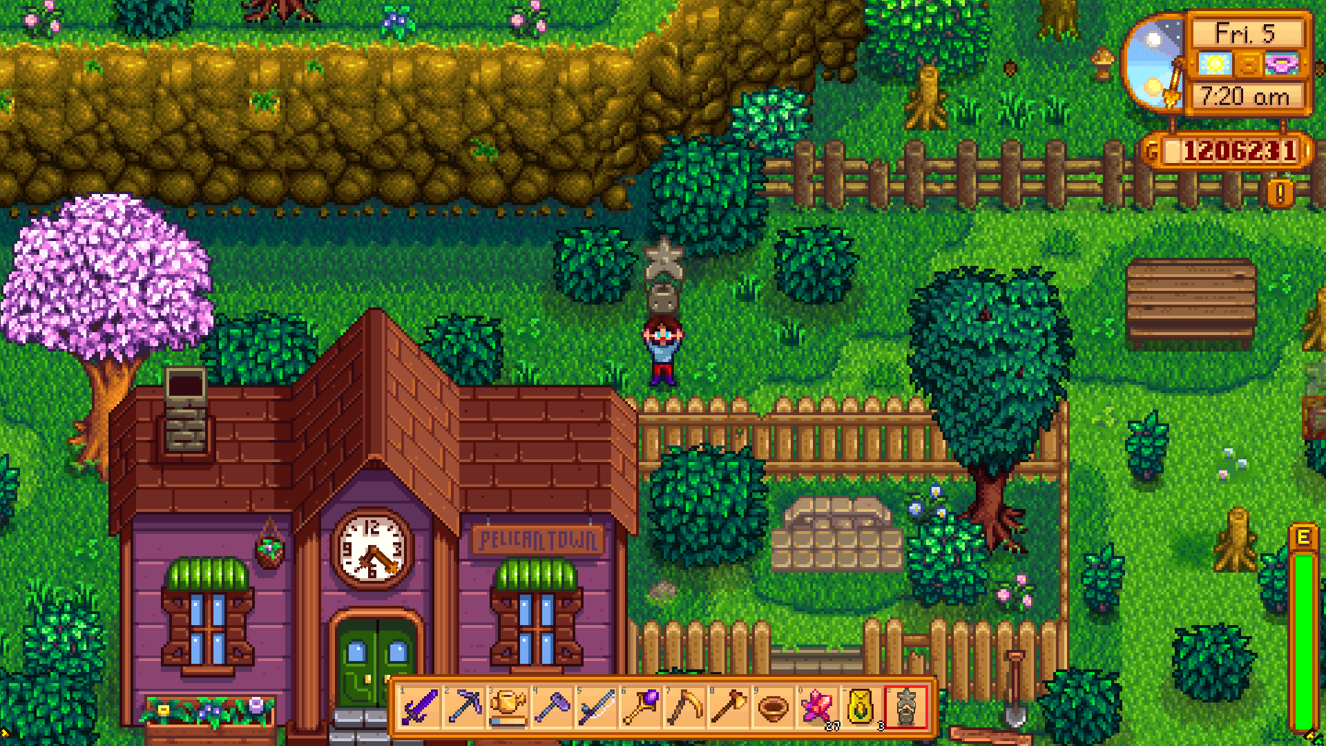 Screenshot of Stardew Valley. The player stands beside the community center. She is holding a stone Junimo statue.
